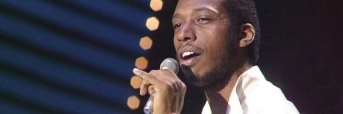 Jeffrey Osborne sorrindo e segurando um microfone durante uma apresentação ao vivo nos anos 80.
