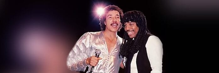 Rick James e Smokey Robinson cantando juntos em um palco com luzes suaves nos anos oitenta.