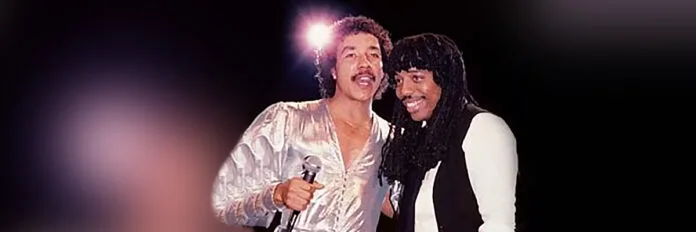 A parceria marcante entre Rick James e Smokey Robinson. Rick James e Smokey Robinson cantando juntos em um palco com luzes suaves nos anos oitenta.