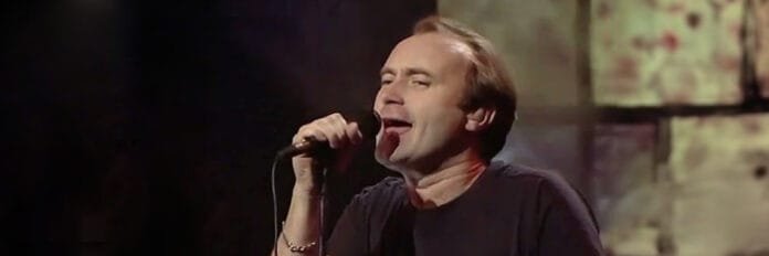 O cantor Phil Collins sorrindo e cantando no microfone a música 