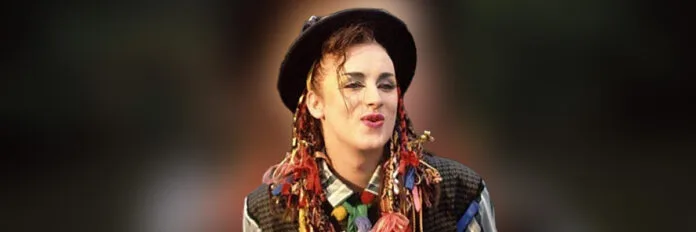 Boy George com visual colorido e chapéu cantando no videoclipe de Karma Chameleon do Culture Club nos anos oitenta.