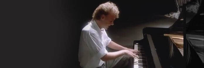 O cantor Bruce Hornsby tocando piano e cantando com sentimento no clipe de The Way It Is nos anos oitenta.