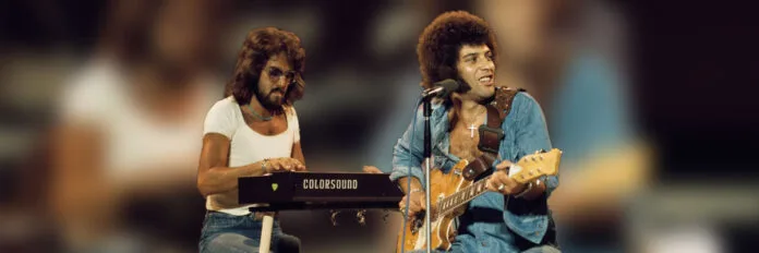 A gravação rústica de In the Summertime e o truque do carro esportivo que mudou a música. Ray Dorset cantando e tocando guitarra acústica com a banda Mungo Jerry no palco em 1970.