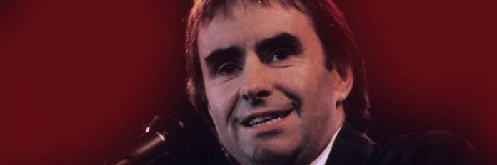 Chris de Burgh segurando o microfone e cantando no palco durante a época do sucesso de The Lady in Red em 1986.