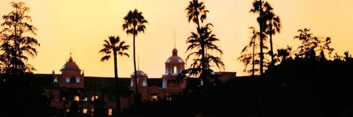 Capa do álbum Hotel California dos Eagles mostrando a fachada iluminada de um hotel ao entardecer com palmeiras e luz dourada